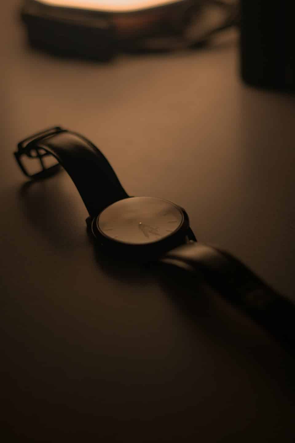 Black wristwatch with a leather strap rests on a surface.