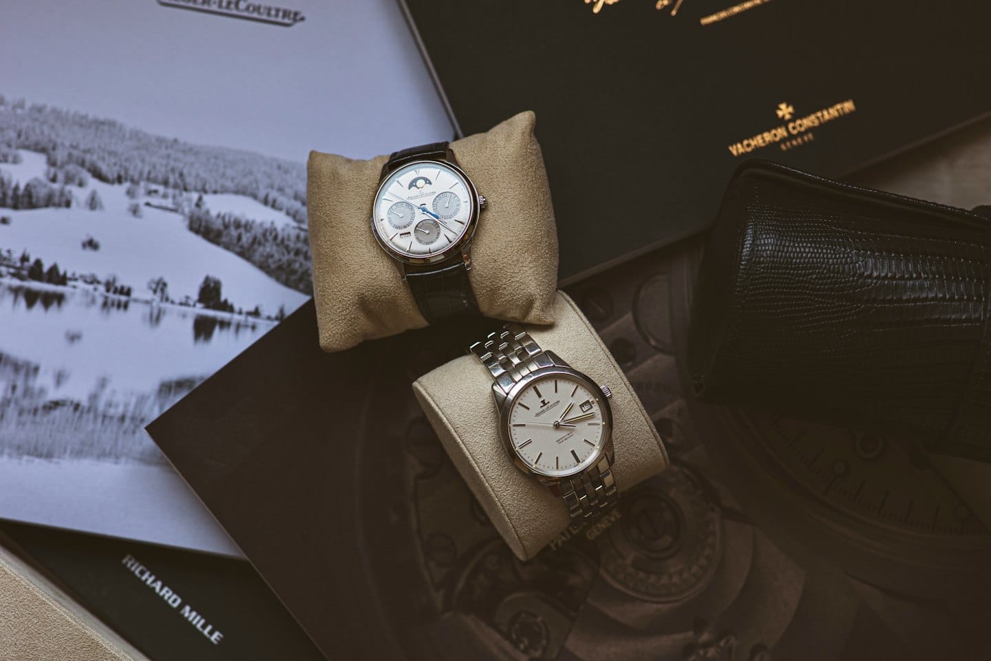Luxury watches displayed on beige suede cushions with branded boxes.